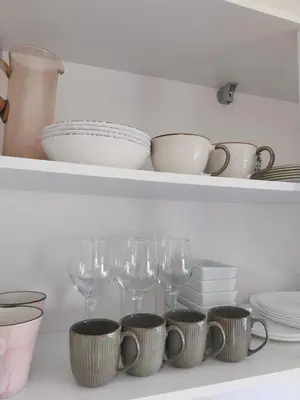 a shelf with plates and wine glasses on it at Saulės miesto apartamentai in Šiauliai