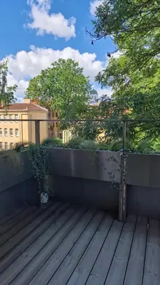 a balcony with a wooden deck with trees and buildings at L18 Apartamentai in Kaunas