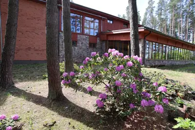 a building with trees and purple flowers in front of it at Poilsiavietė - kempingas ''Viktorija''