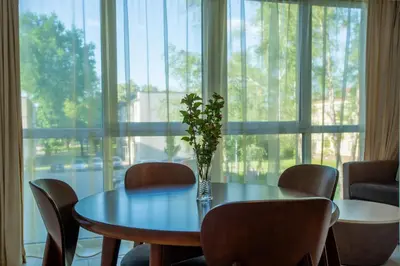 a table with a vase of flowers on it in front of a window at Park apartment in Druskininkai