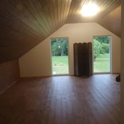 an empty room with two windows and wood floors at Draugų sodyba