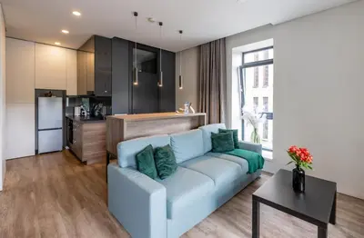 a living room with a blue couch and a kitchen at Vincent Urban Nest - Near Clinic, Arena and Stadium in Kaunas