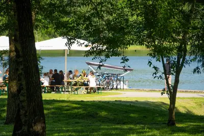 a group of people sitting at tables by the water at Saulės laikrodžio apartamentai in Šiauliai