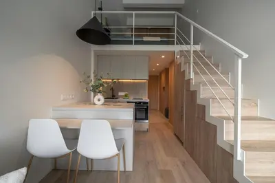 a kitchen with white chairs and a staircase at Loft 12 in Vilnius