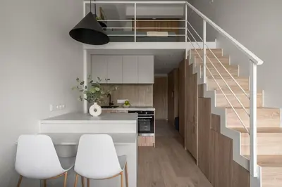 a kitchen with a staircase and white counters and white chairs at Loft 12 in Vilnius