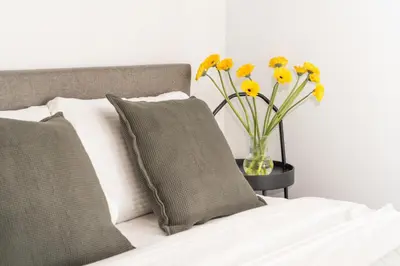 a vase filled with yellow flowers sitting next to a bed at Cinema Loft - Self Check in in Vilnius