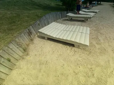 a white bench sitting in the sand next to a fence at Light House in Vilnius