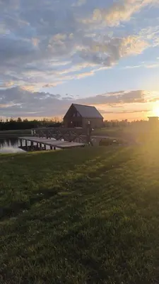 a barn in a field with the sun setting at Baltasis beržas