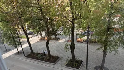 two people sitting on a bench under some trees at Avenue Apartments in Kaunas