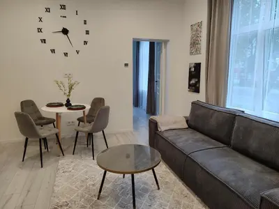 a living room with a couch and a table and a clock at UrbanHome Rokiškis in Rokiškis