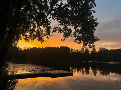 a sunset over a lake with a wooden dock at Glamp Juodis in Ubiškės
