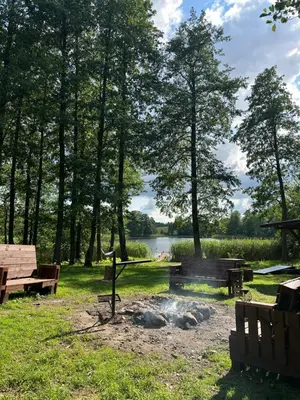 a fire pit in a park with benches and a lake at Glamp Juodis in Ubiškės