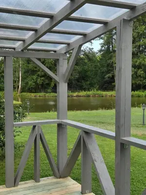 a wooden pergola in a park with a pond at Sodyba Upulupu