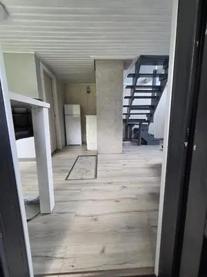 an empty room with a wooden floor and a refrigerator at Sodyba Upulupu