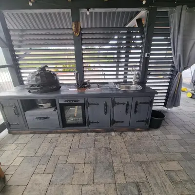 an outdoor kitchen with a table in front of a window at Sodyba Pirtis Panarvė in Lazdijai
