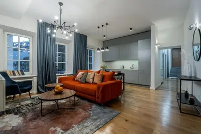 a living room with an orange couch and a kitchen at Domillion new modern 2bdr City Hall apt D1117B in Vilnius