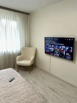 a bedroom with a tv on the wall and a chair at Cozy Šmozy Apartamentai in Šiauliai