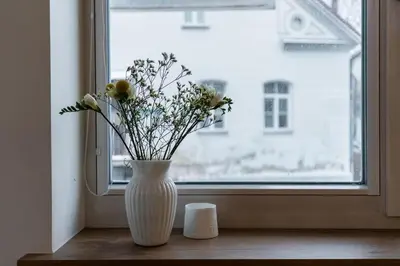 a white vase with flowers sitting on a window sill at Domillion 1bdr lovely apt with parking &lift B9a4 in Vilnius
