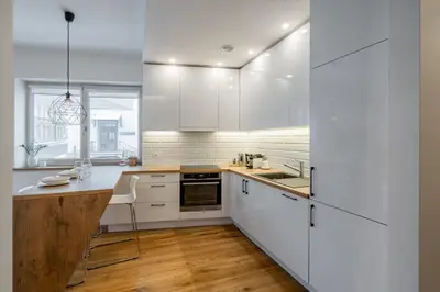 a kitchen with white cabinets and a wooden floor at Domillion 1bdr lovely apt with parking &lift B9a4 in Vilnius