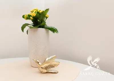 a white vase with flowers and a gold bird statue at SarkuGuzta Cozy Apartment in Kaunas