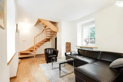 a living room with a black leather couch and a staircase at Saint John Two Bedroom Cottage by Reside Baltic in Vilnius