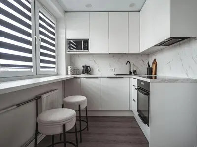 a white kitchen with white cabinets and stools at Feliz Stay in Šiauliai