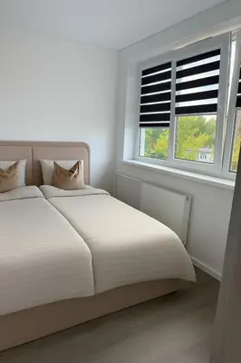 a white bedroom with a bed and two windows at Feliz Stay in Šiauliai