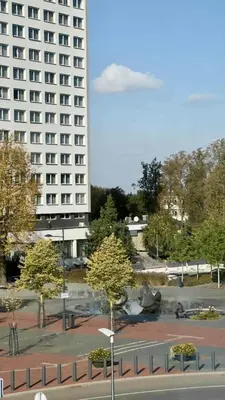 a large white building with a parking lot with trees at Draugystės Apartments - Šiauliai Center in Šiauliai