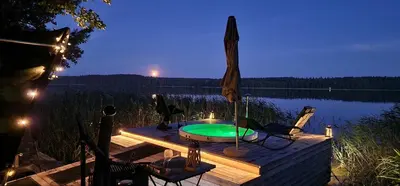 a hot tub on a deck next to a lake at night at Lakajų Resort in Molėtai