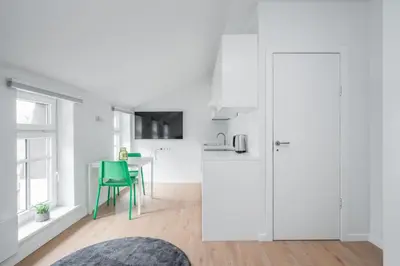 a white kitchen with a table and a green chair at LUMA Apartments by Reside Baltic in Vilnius