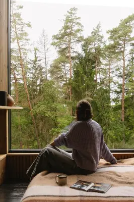 a man sitting on a bed looking out of a window at Blackview cabin in Kulautuva