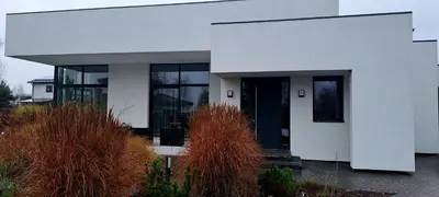 a white house with a black door and some bushes at White house in Vilnius in Vilnius