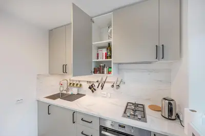 a white kitchen with white cabinets and a sink at Cozy airport apartment