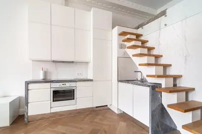 a kitchen with white cabinets and a spiral staircase at Old Town Luxury apartment self check inn in Vilnius