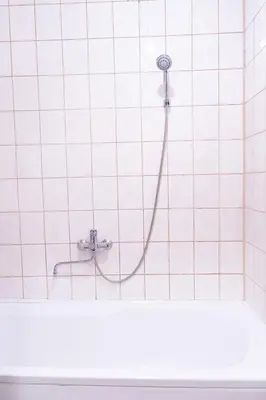 a shower with a hose in a white tiled bathroom at Vilnius Old Town Riverside Apartment in Vilnius
