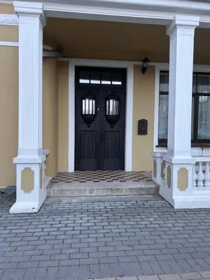 a black door on a yellow house with columns at Vydūno apartamentai in Kaunas