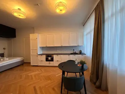 a room with a table and a kitchen with white cabinets at Vydūno apartamentai in Kaunas