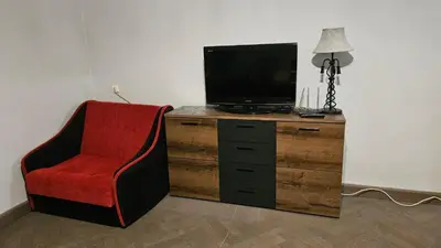 a tv sitting on top of a wooden dresser with a red chair at Dviejų kambarių butas Kauno centre in Kaunas