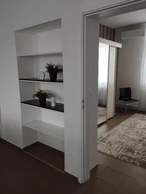 a hallway with white shelves and a room with a chair at XXL apartamentai su nemokamu parkingu in Šiauliai