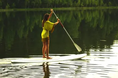 a woman standing on a paddle board in the water at namelis tyloje in Šarkiškės
