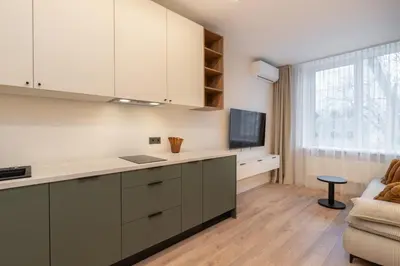 a kitchen with white cabinets and a tv and a couch at City Rooms by Lollo Stay in Vilnius