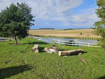 a field with a fence and a lake with logs at Šaltenių pašvaistė