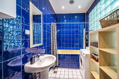 a blue tiled bathroom with a sink and a mirror at Guido apartament in Šiauliai