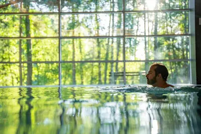 a man is swimming in a pool with a window at UPA Medical SPA in Druskininkai