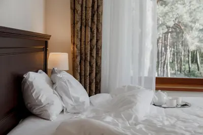 a bed with white sheets and pillows next to a window at Pušynė in Birštonas