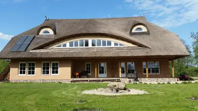 a house with a thatched roof on top of a yard at Vila Sanzila in Bernatoniai
