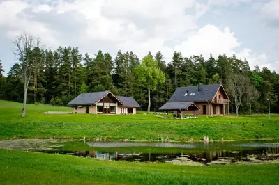 a house in a field next to a pond at Harmony Park Countryside Villas & SPA in Prienai