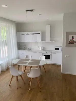 a white kitchen with a table and white chairs at Apartamentai Fortuna in Kaunas