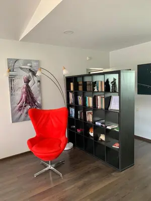 a red chair in a room with a book shelf at Apartamentai Fortuna in Kaunas