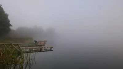 a dock in the middle of a lake in the fog at Trainiškio pirkia in Ginučiai